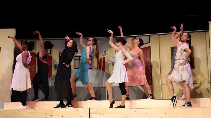 Eine Gruppe von Schülerinnen und Schülern der Pierrefonds Community High School steht auf der Bühne und hebt die Arme in einer Tanzpose.