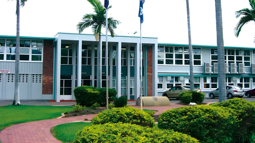 Das moderne mehrstöckige Gebäude mit großen Fenstern der Pimlico State High School ist von grüner Vegetation mit Palmen umgeben.