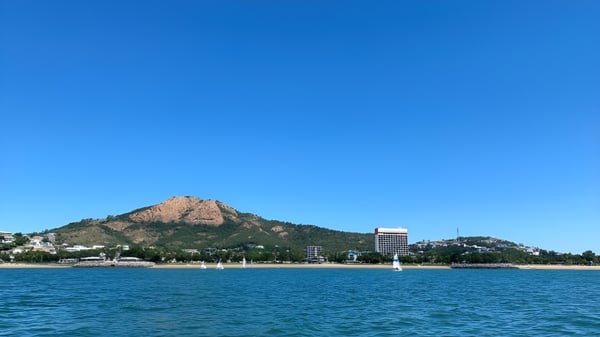 Eine felsige Bergspitze ragt über einem ruhigen See mit Gebäuden im Hintergrund auf dem Gelände der Pimlico State High School auf.