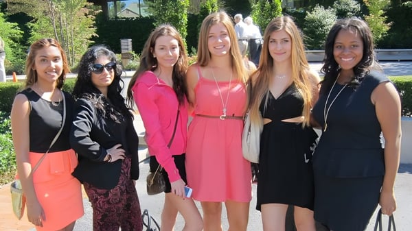 Eine Gruppe von sechs Schülerinnen steht im Freien auf dem Campus der Pine Ridge Secondary School vor einem Gebäude und grüner Umgebung.