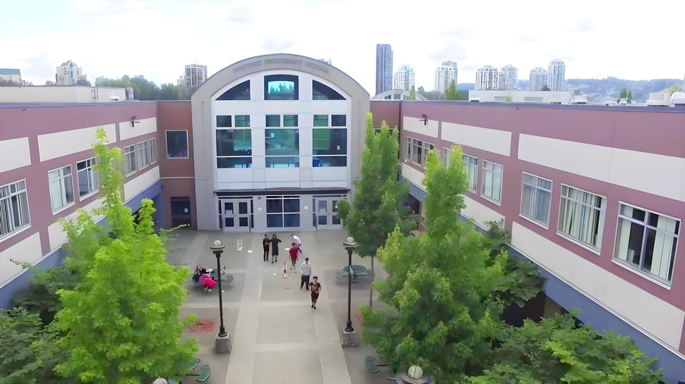 Das moderne mehrstöckige Hauptgebäude mit einem Rundbogen-Eingang der Pinetree Secondary School ist von Grünflächen umgeben.