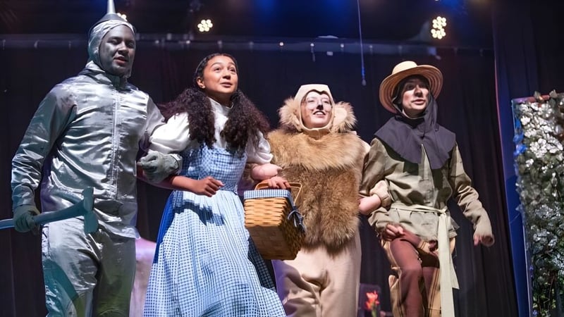 Vier Schüler der Pinewood Preparatory School stehen kostümiert auf der Bühne vor einer beleuchteten Kulisse.