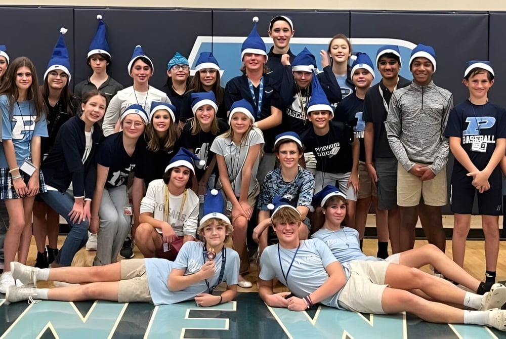 Eine Gruppe von Schülerinnen und Schülern der Pinewood Preparatory School steht gemeinsam in der Sporthalle mit verschiedenen Sportgeräten im Hintergrund.