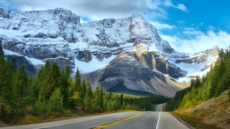 Eine gewundene Straße führt durch ein bewaldetes Tal zu schneebedeckten Bergen auf dem Campus der Pitt Meadows Secondary School.