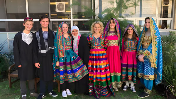 Eine Gruppe von Frauen in bunten, traditionellen Kleidern steht vor einem Gebäude auf dem Campus der Pittwater High School.
