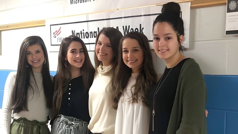 Fünf Schülerinnen stehen vor einer Wand mit dem Schriftzug National Math Week auf dem Campus der Pleasant Valley High School.