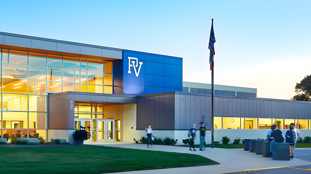 Das moderne mehrstöckige Gebäude der Pleasant Valley Secondary School mit blauer Fassade und großen Fenstern wird von einem Rasen und Personen vor dem Eingang umgeben.