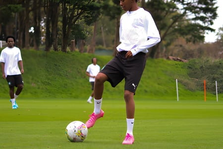 Ein Schüler des Plymouth College dribbelt einen Fußball auf einem Rasenfeld mit weiteren Spielern im Hintergrund.