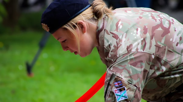 Eine Person in militärischer Tarnuniform steht auf einer Wiese auf dem Gelände des Plymouth College mit gesenktem Kopf.