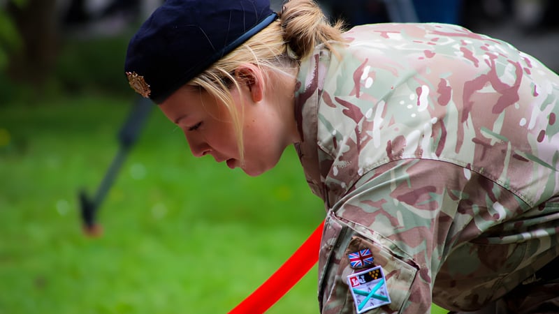 Eine Person in militärischer Tarnuniform steht auf einer Wiese auf dem Gelände des Plymouth College mit gesenktem Kopf.