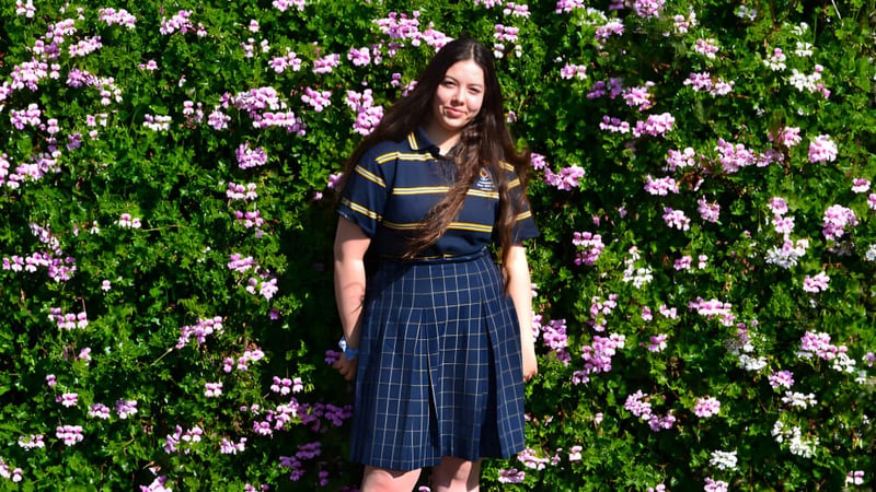 Eine junge Frau steht in einem grünen Garten mit blühenden rosa Blumen auf dem Gelände des Plympton International College.