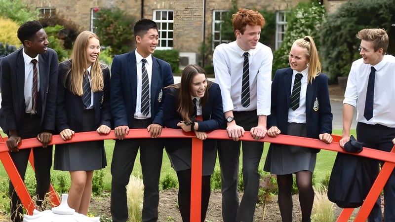 Eine Gruppe Schüler der Pocklington School steht auf einer roten Brücke vor einem Backsteingebäude im Freien.