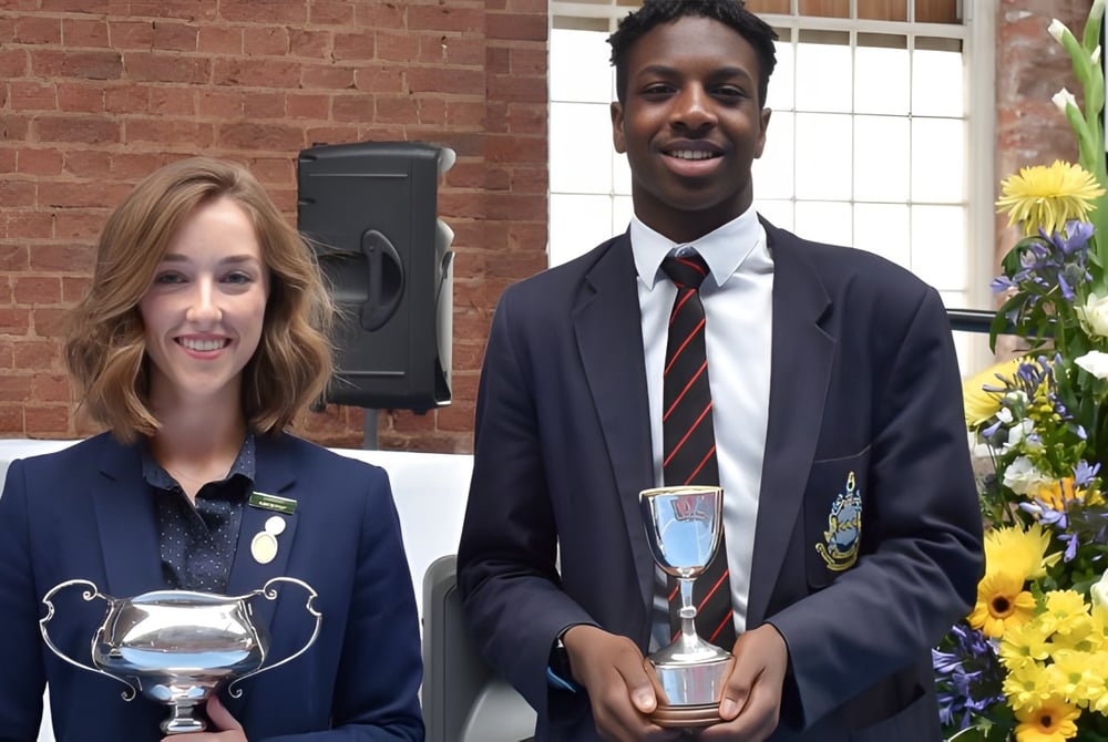 Zwei Personen in formeller Kleidung halten Trophäen bei einer Siegerehrung auf dem Campus der Pocklington School.