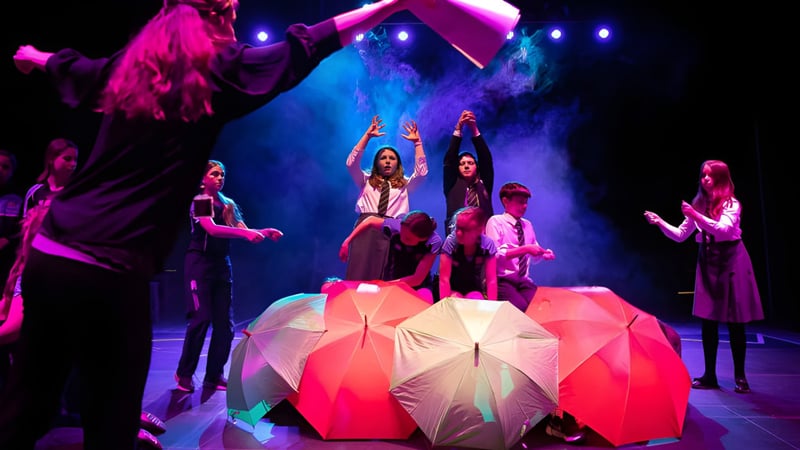 Schüler der Pocklington School führen eine Tanzaufführung mit bunten Kostümen und Regenschirmen auf einer Bühne mit dramatischer Beleuchtung auf.