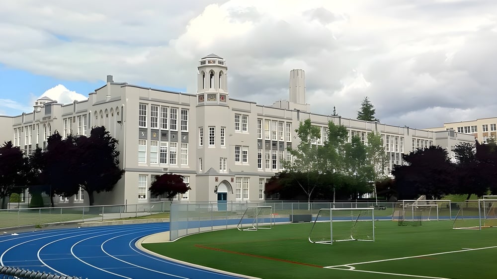 Das große Gebäude der Point Grey Secondary School mit Uhrenturm steht hinter dem Sportfeld mit Laufbahn und Fußballtoren.