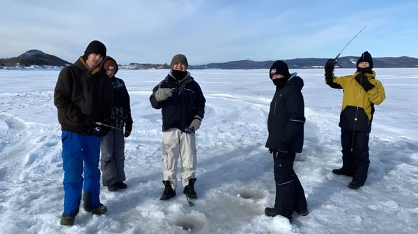 Eine Gruppe Schüler der Polyvalente Roland-Pépin steht in Winterkleidung auf einem zugefrorenen See vor Bergkulisse.