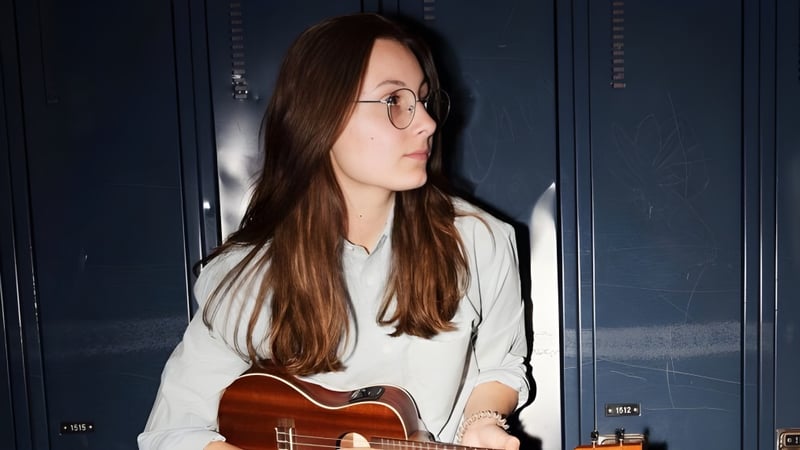 Eine Schülerin der Polyvalente Roland-Pépin hält eine akustische Gitarre vor einer dunkelblauen Wand.