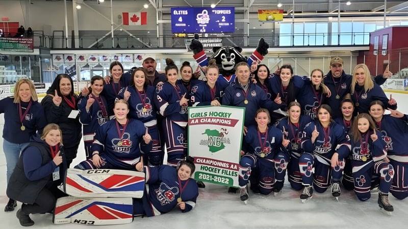 Die Damen-Eishockeymannschaft der Polyvalente Thomas-Albert steht in ihren blauen Trikots in der Eishalle vor kanadischer und britischer Flagge.