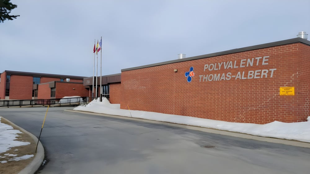 Das Backsteingebäude der Polyvalente Thomas-Albert ist von einer verschneiten Landschaft umgeben und ein Fahnenmast steht im Vordergrund.