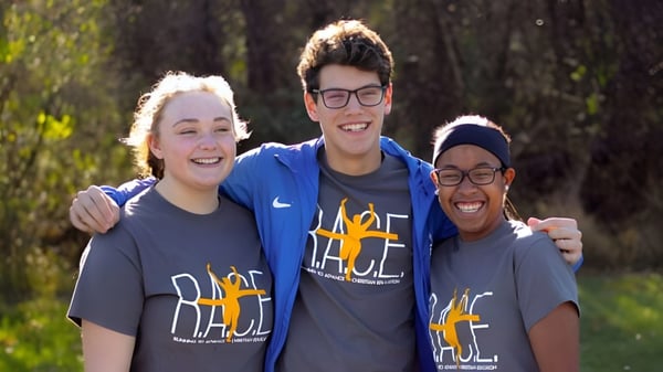 Drei Schülerinnen und Schüler stehen lächelnd im Wald auf dem Gelände der Portland Christian High School.