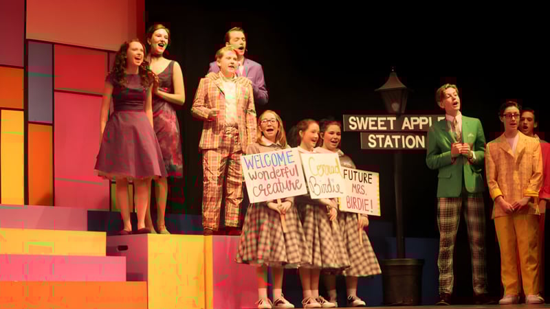 Eine Gruppe von Schülern steht auf der Bühne des Portlaoise College bei einer Veranstaltung mit dem Schild Sweet Apple Station im Hintergrund.