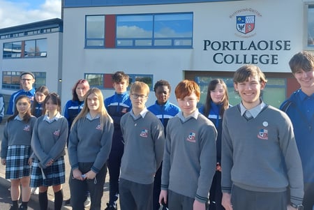 Schüler des Portlaoise College stehen vor einem modernen Schulgebäude mit großen Fenstern.