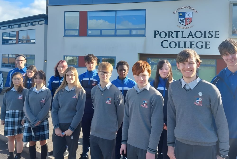 Schüler des Portlaoise College stehen vor einem modernen Schulgebäude mit großen Fenstern.