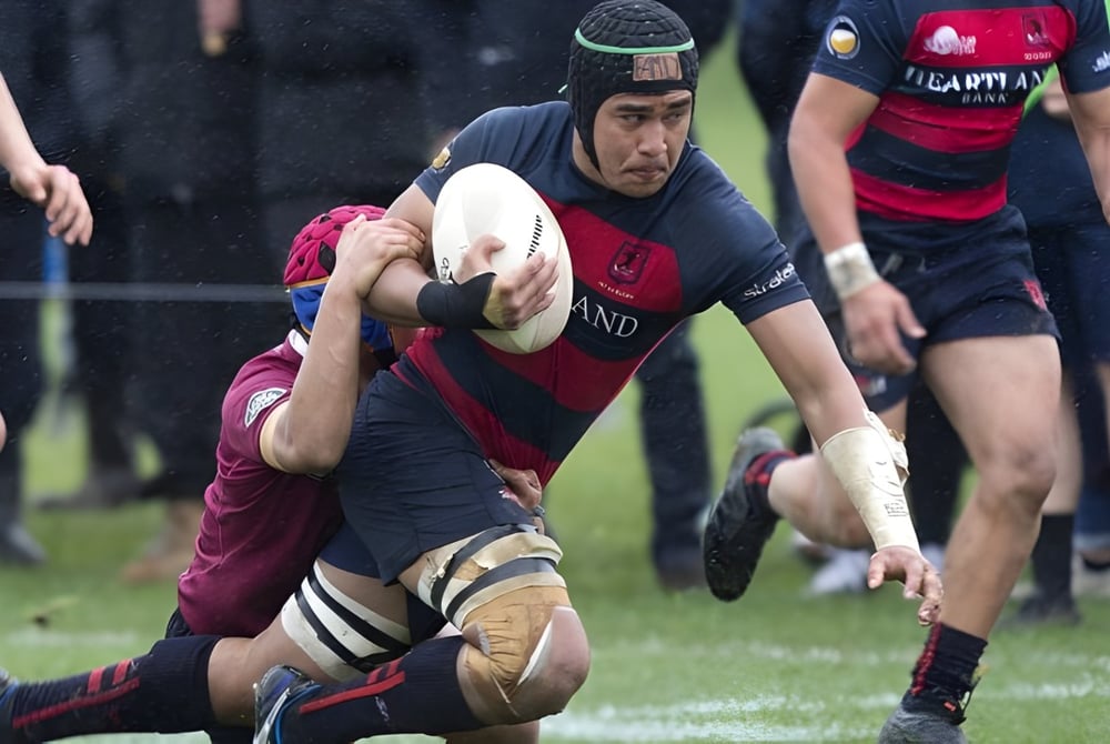 Ein Rugbyspieler der Portmarnock Community School trägt den Ball, während er auf dem Spielfeld von einem Gegenspieler getackelt wird.
