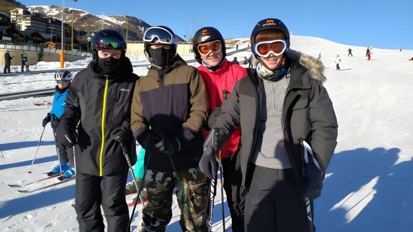 Eine Gruppe von vier Schülerinnen und Schülern der Portmarnock Community School steht in Winterkleidung auf einem verschneiten Hang vor Bergen.