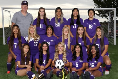 Eine Gruppe junger Fußballspielerinnen in lila Trikots mit ihrem Trainer auf dem Spielfeld des Portsmouth College.