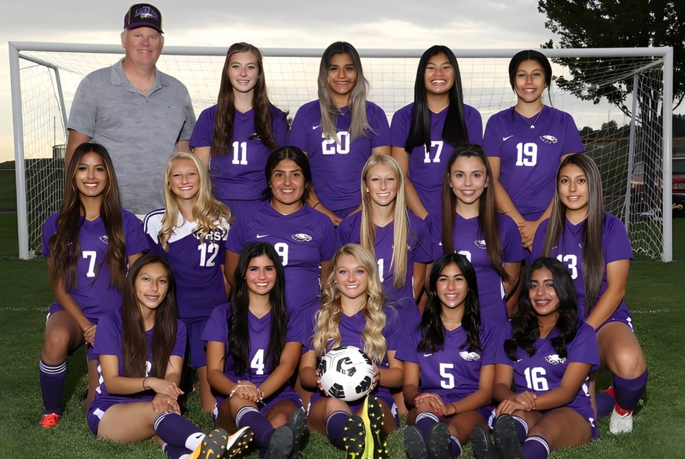 Eine Gruppe junger Fußballspielerinnen in lila Trikots mit ihrem Trainer auf dem Spielfeld des Portsmouth College.