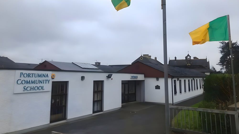 Das Gebäude des Portumna Community College mit einer Flaggen-Dekoration außen, umgeben von einer Grasfläche unter bewölktem Himmel.