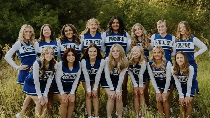 Eine Gruppe Cheerleader in blauen und weißen Uniformen posiert auf einem Feld auf dem Campus des Poudre School District.