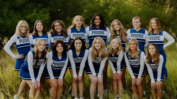 Eine Gruppe junger Schülerinnen im Cheerleading-Uniform posiert zusammen auf einer Wiese im Poudre School District.
