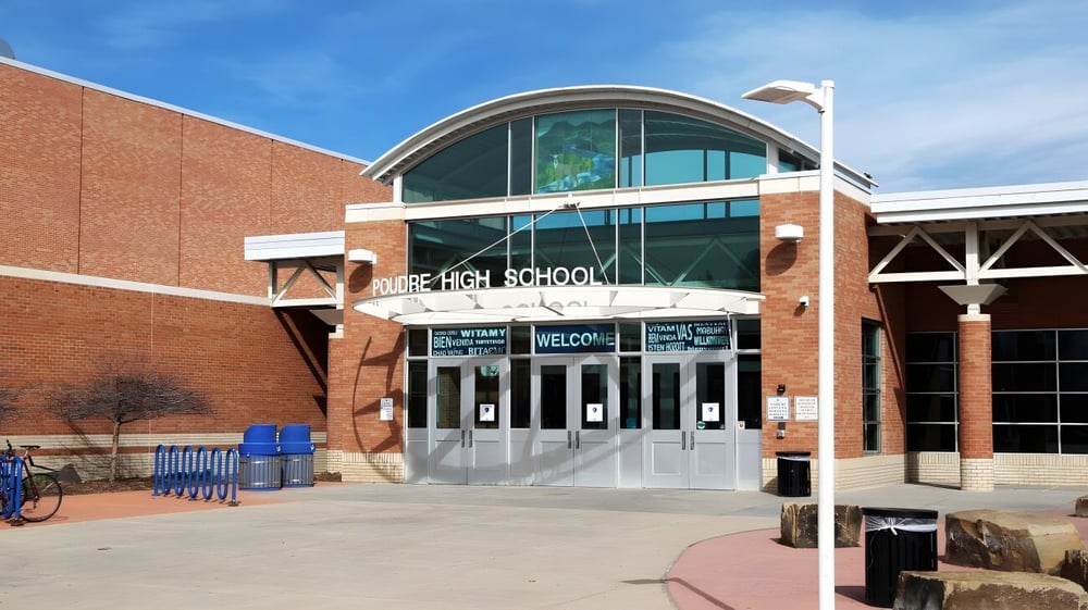 Das Backsteingebäude mit großem Bogen am Eingang gehört zum Poudre School District und steht unter klarem blauem Himmel.
