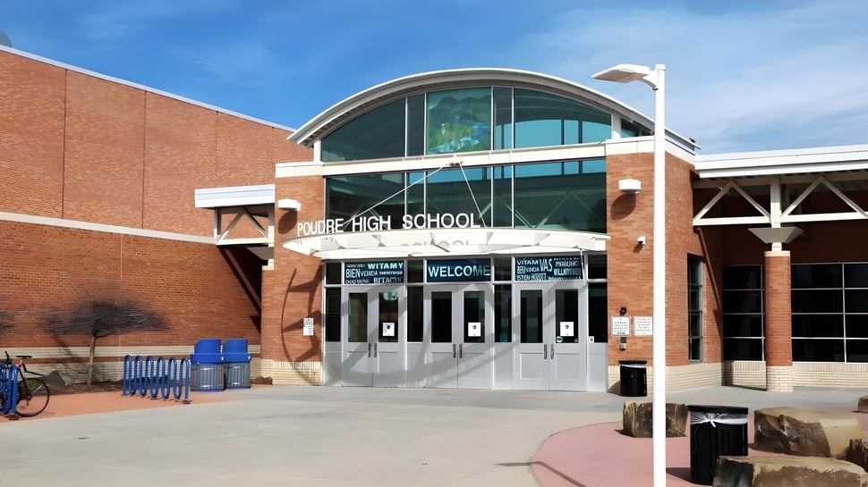 Das Backsteingebäude mit einem gewölbten Glaseingang im Poudre School District ist von einem gepflasterten Bereich mit Bänken und einem Fahrradständer umgeben.