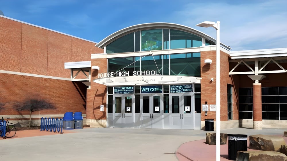 Das Backsteingebäude mit einem gewölbten Glaseingang im Poudre School District ist von einem gepflasterten Bereich mit Bänken und einem Fahrradständer umgeben.