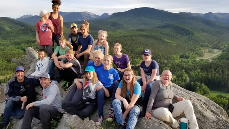 Eine Gruppe von Schülerinnen und Schülern sowie Erwachsenen der Prairie Christian Academy steht auf einem Felsen und blickt auf bewaldete Berge.
