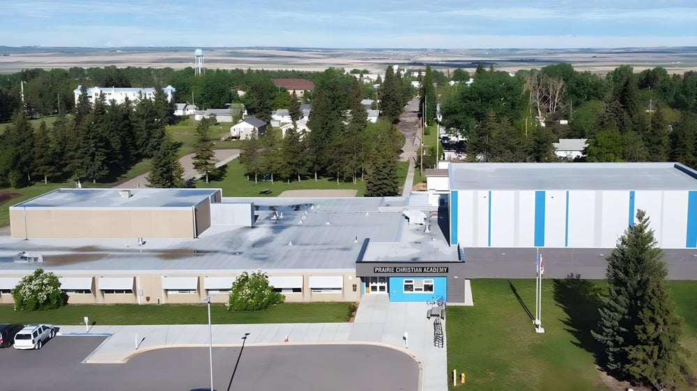 Das moderne Hauptgebäude der Prairie Christian Academy steht vor einer Wiese mit Wald im Hintergrund unter blauem Himmel.