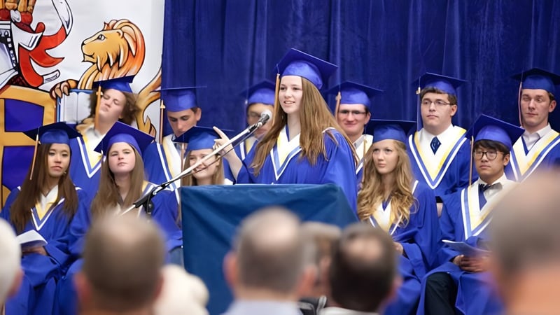 Absolventinnen und Absolventen der Prairie Christian Academy stehen in blauen Talaren auf der Bühne vor einem blauen Vorhang.
