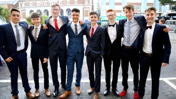 Eine Gruppe von Schülern des Presentation Brothers College steht formell gekleidet vor einem Backsteingebäude.