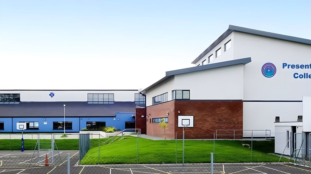 Das moderne mehrstöckige Schulgebäude des Presentation College Carlow mit blau-weißem Äußeren, umgeben von Grünfläche und Zaun.