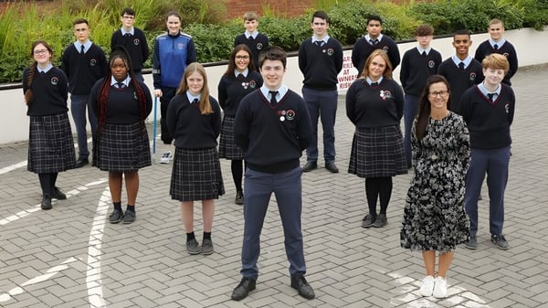 Eine Gruppe Schülerinnen und Schüler des Presentation College Carlow steht zusammen auf einem gepflasterten Außenbereich mit Grünflächen.