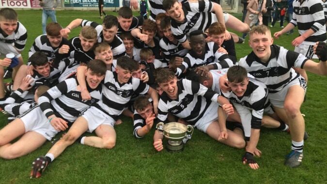 Schüler des Presentation College Carlow feiern auf einem Feld und halten einen Pokal hoch.