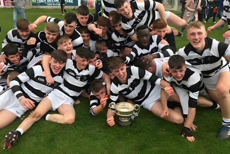 Schüler des Presentation College Carlow feiern auf einem Feld mit einem Pokal in der Hand.