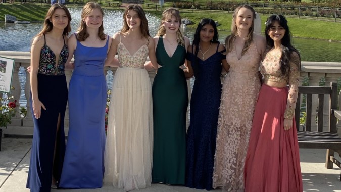 Sechs Schülerinnen der Presentation Secondary School Thurles stehen in Abendkleidern vor einer malerischen Wasser- und Waldkulisse.