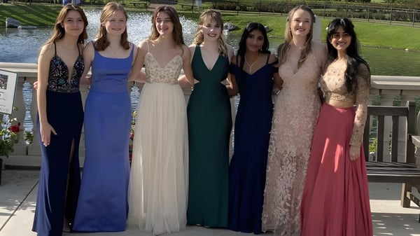 Eine Gruppe Schülerinnen der Presentation Secondary School Thurles steht in Abendkleidern vor einer landschaftlichen Kulisse mit Wasser.