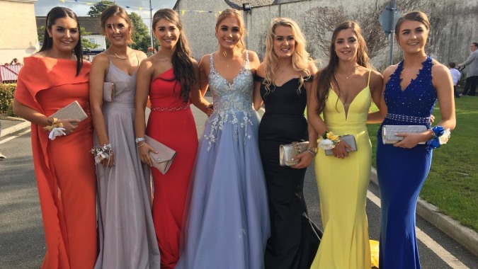 Eine Gruppe junger Frauen in eleganten Abendkleidern posiert draußen vor Gebäuden auf dem Gelände der Presentation Secondary School Kilkenny.