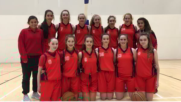 Schülerinnen der Presentation Secondary School (Cork) stehen gemeinsam in der Sporthalle in ihren roten Basketball-Trikots.