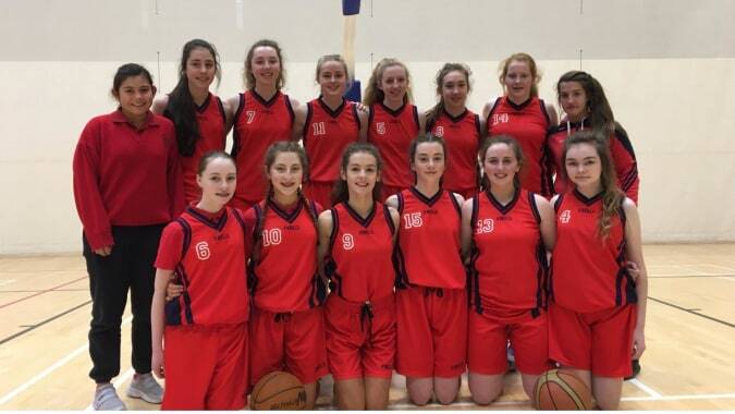 Eine Gruppe junger Basketballspielerinnen in roten Trikots posiert in der Turnhalle der Presentation Secondary School in Cork.